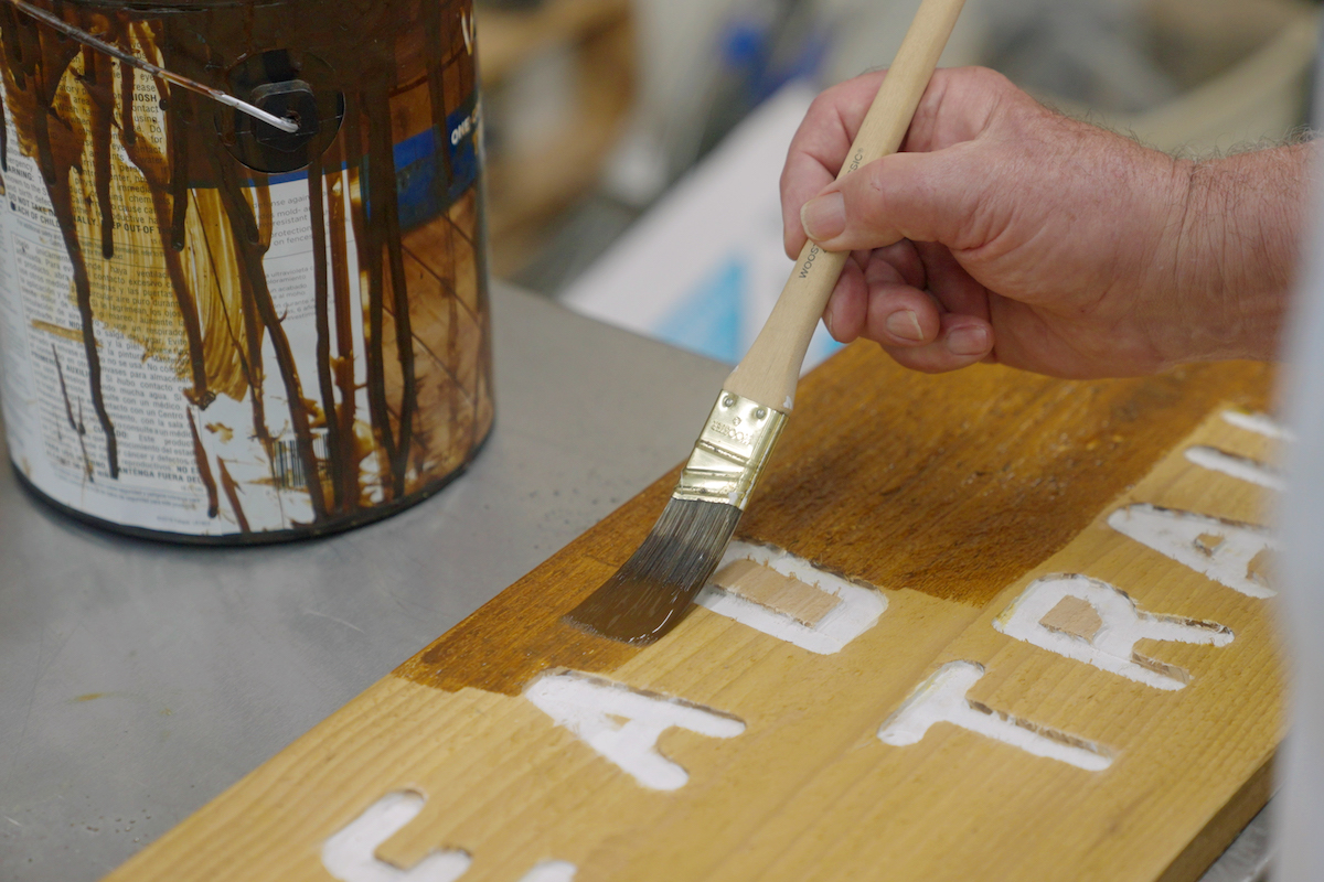 Senior Man Applies Stain to Wooden Sign_Uplands Village