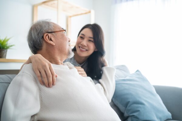 Asian Daughter Hugs Senior Father From Behind the Couch_Uplands Village