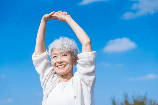 A senior woman stretching outside with a smile.