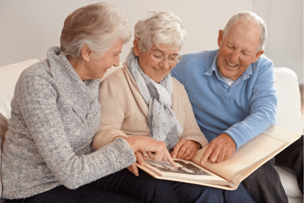 A group of elderly people gather together in the living room, fondly flipping through a photo album filled with cherished memories.