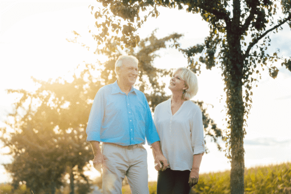 An elderly couple strolling along a peaceful countryside path as the sun sets in the evening.